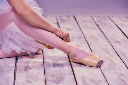 Professional ballerina putting on her ballet shoes on the wooden floor on a pink background. feet close-upの写真素材