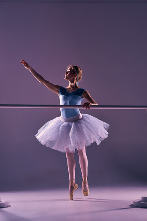classic ballet dancer in white tutu at ballet barre on a lilac backgroundの写真素材
