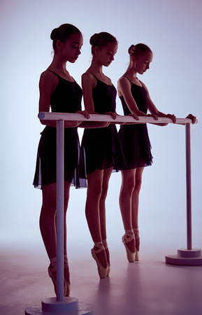 Three young ballerinas stretching on the bar on lilac backgroundの写真素材