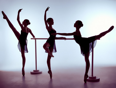 Three young ballerinas stretching on the bar on lilac backgroundの写真素材