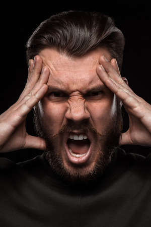 Portrait of young frightened  crying man with a beard and mustache in studio on black background. concept of rageの写真素材