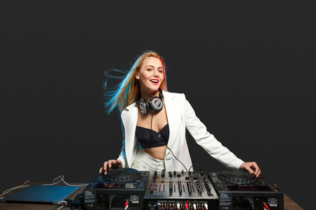 Beautiful blonde DJ girl in a white suit on decks on the party on the black backgroundの写真素材