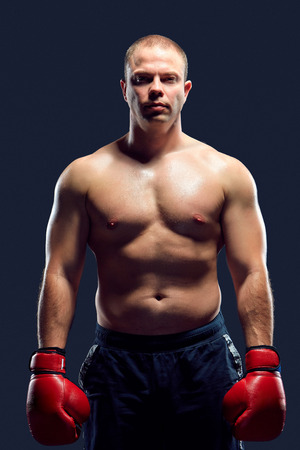 Muscular man - young caucasian boxer in red gloves standing over black background. arms down down and along the bodyの写真素材