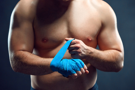 Vertical shot of a muscular boxer bandaging his hands on gray backgroundの写真素材