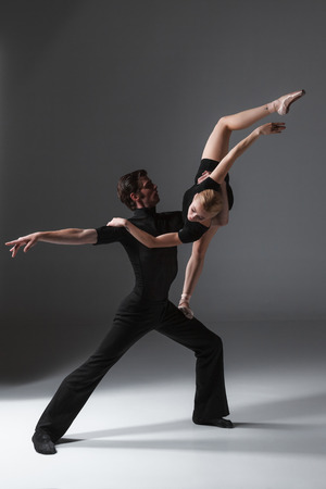 The two young modern ballet dancers in black suits posing over gray studio backgroundの写真素材