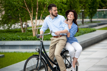 Young couple sitting on a bicycle opposite the green city parkの写真素材