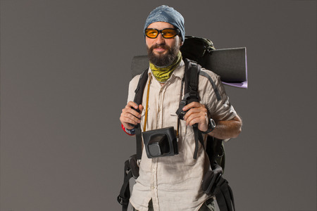 Portrait of a male fully equipped tourist with backpack and the camera on gray backgroundの写真素材