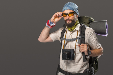 Portrait of a male fully equipped tourist with backpack and the camera on gray backgroundの写真素材