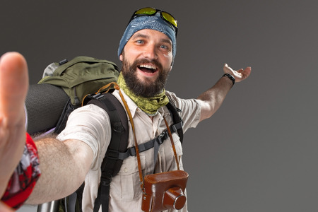Portrait of a male smiling fully equipped tourist with backpack and the camera on gray background. tourist opened his arms, inviting travelの写真素材