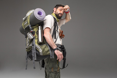 Portrait of a male fully equipped tourist with backpack and the camera on gray background. side view. tourist looking into the camera and  wiping sweatの写真素材