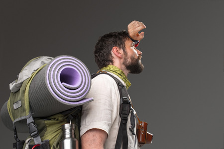 Portrait of a male fully equipped tourist with backpack and the camera on gray background. side view. tourist  wiping sweatの写真素材