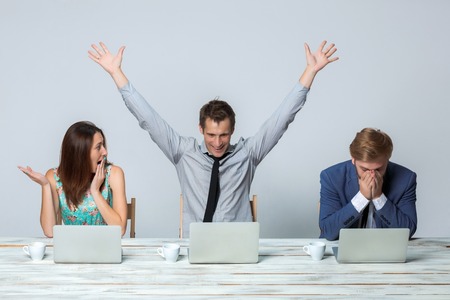 Business team working together at office on light gray background. all working on laptops. One man raising his arms enjoying good ideaの写真素材