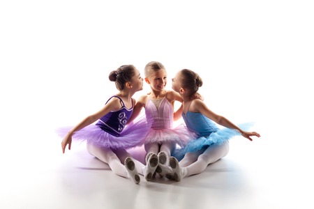 Three little ballet girls sitting  in multicolored tutu and pointe shoes together on white backgroundの写真素材