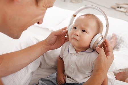 young father with his nine months old som on the bed at home on white background. Father and son wearing headphonesの写真素材