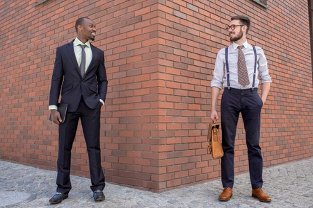 Portrait of multi ethnic business team. Two happy smiling men standing against the backdrop of the city. The one man is African-American, other is European. concept of business success and old and new business formationの写真素材