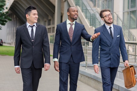Portrait of multi ethnic business team.Three smiling men walking against the background of city. The one man is European, other is Chinese and African-American.の写真素材