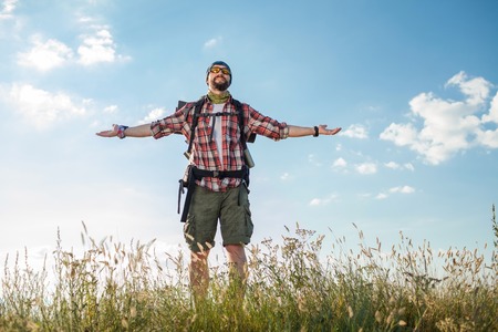 Young smilimg caucasian tourist with backpack  standing on the top of hill against blue skyの写真素材