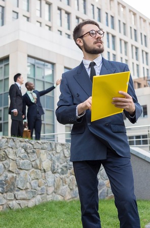 Portrait of multi ethnic business team.Three men standing against the background of red brick wall. The foreground of a European man. Other men is Chinese and African-American. The concept of doubt in the success of the transactionの写真素材