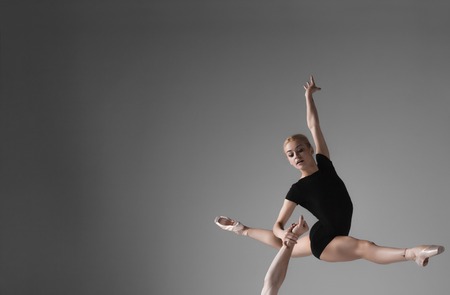 The young modern ballet dancers in black suits over gray studio background.  Ballerina jumping on the arm of a partnerの写真素材