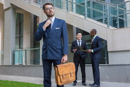 Portrait of multi ethnic business team.Three men standing against the background of city. The foreground of a European man. Other men is Chinese and African-American. The concept of success of the transactionの写真素材