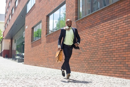 The african man as black businessman with a briefcase running in a city street on a background of red brick wallの写真素材