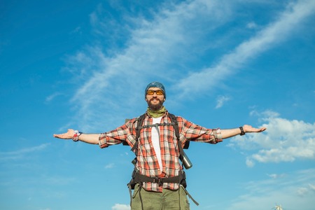 Young smilimg caucasian tourist with backpack  standing on the top of hill against blue sky background. The concept of an invitation to travelの写真素材