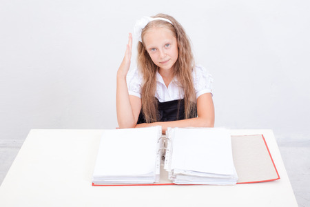 Schoolgirl  with red folders sitting at the table over white backgroundの写真素材