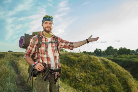 Young smilimg caucasian tourist with backpack  standing on the top of hill and looking at the camera. The concept of an invitation to travelの写真素材