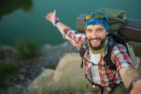 Young smilimg caucasian tourist with backpack  standing on the top of hill and looking at the camera. The concept of an invitation to travelの写真素材