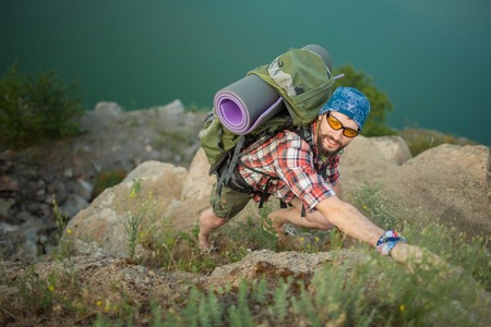 Young smilimg caucasian tourist with backpack climbing the rock and looking at the cameraの写真素材