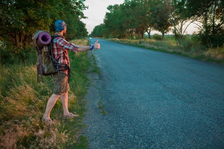 Young caucasian tourist with backpack hitchhiking along a road in sunsetの写真素材