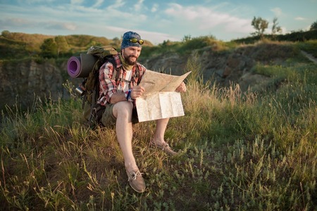 Young smilimg caucasian tourist with backpack sitting on the top of hill in green grass and...