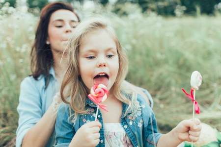 The young mother and daughter with candies on green grass backgroundの写真素材