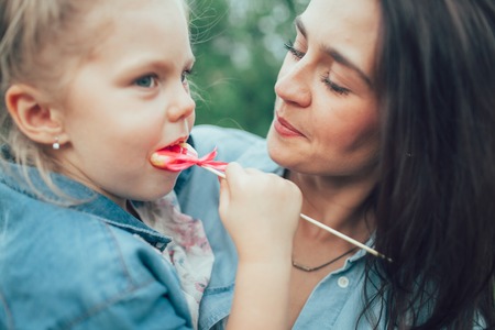 The young mother and daughter with candies on green grass backgroundの写真素材