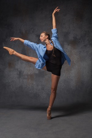 The young beautiful modern style dancer in a blue shirt posing on a studio gray backgroundの写真素材