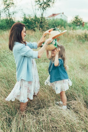 The side view of young mother and daughter with hats on green grass backgroundの写真素材