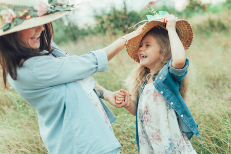 The side view of young mother and daughter with hats on green grass backgroundの写真素材