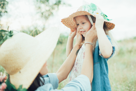 The side view of young mother and daughter with hats on green grass backgroundの写真素材