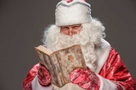 happy Santa Claus in eyeglasses reading old book on black backgroundの写真素材