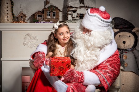 holidays, celebration, childhood and people concept - smiling little girl with santa claus over christmas tree  backgroundの写真素材