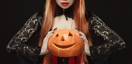 Girl in witch costume with Halloween pumpkin on black background