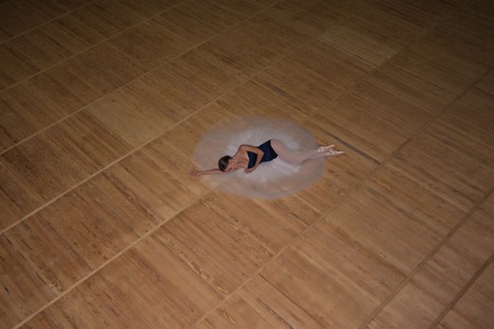 The beautiful ballerina lying in long white skirt on wooden floor backgroundの写真素材