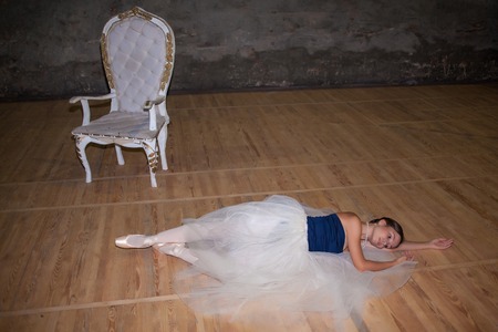 The beautiful ballerina lying in long white skirt on wooden floor backgroundの写真素材