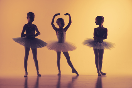 The silhouettes of little ballerinas in dance studio posing on a orange backgroundの写真素材