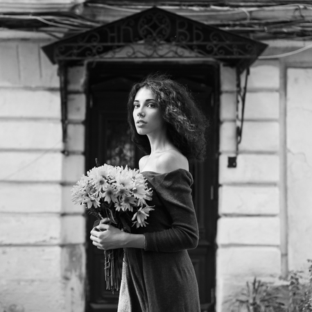 Fashion style colorless photo of a young woman with flowers on a city backgroundの写真素材