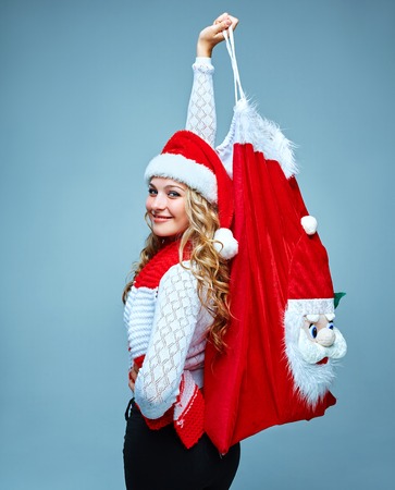Girl dressed in santa hat  holding a Christmas decoration  Bag of Santa Claus and looking at camera. Holiday concept with blue background.の写真素材
