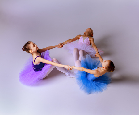 Three little ballet girls sitting  in multicolored tutus and pointe shoes together on lilac backgroundの写真素材