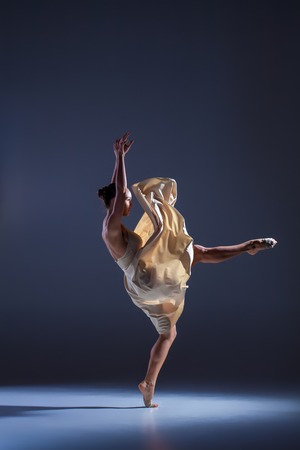 Young beautiful dancer in beige dress dancing on gray studio backgroundの写真素材