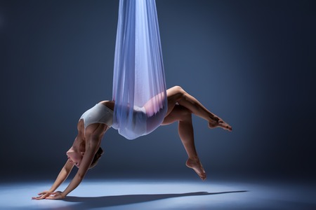 Young beautiful dancer in beige dress posing with  hammock fabric on gray studio backgroundの写真素材