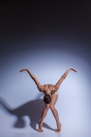 Young beautiful dancer in beige swimwear dancing on lilac studio backgroundの写真素材